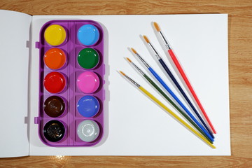 Naklejka premium Blank sketchbook, set of watercolor paints and brushes on a wooden table