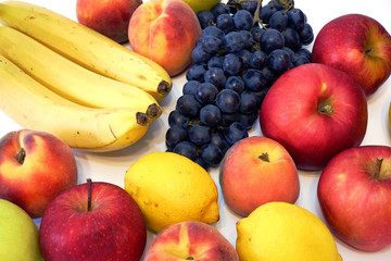 Fresh juicy fruits: bananas, black vine grapes, red apples, peaches, lemons