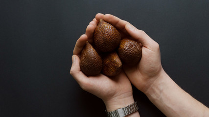 salak fruit in hands on dark background