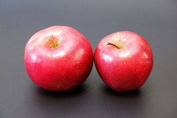 Two tasty juicy red apples with shadow on dark gray background close up view