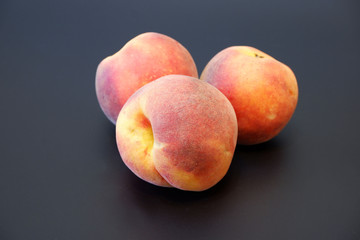Fototapeta na wymiar Three juicy ripe peaches on dark gray background cluse up view