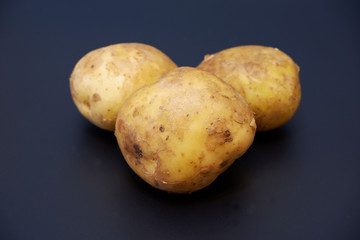 Three organic potatoes on dark gray matte background close up view