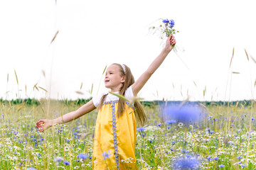 Little pretty girl in yellow Russian dress picking flowers in field of wild flowers on summer day.