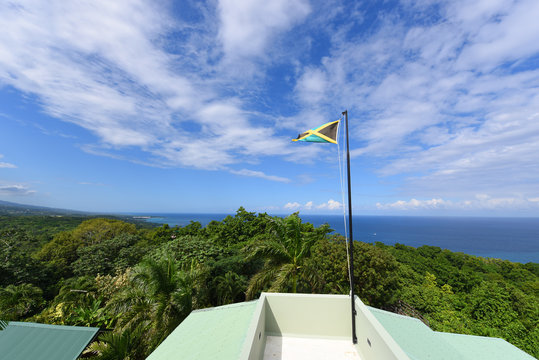 Flag of Jamaica waving against blue sky. Flag of Jamaica have a gold saltire on a green and black field.