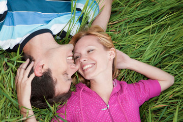 Young loving couple lying on green grass