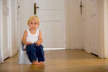 Infant child baby boy toddler sitting on potty, playing with toys in living room