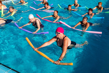 Senior ladies working out in pool with foam noodles.