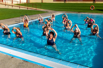 Senior women doing warmup exercises in outdoor pool.