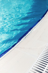 Blue water with light reflection at the edge of the curved swimming pool. The concept of summer travel and recreation