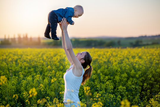 Young mother holding up her todller son in canola field
