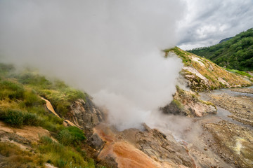 Geyser eruption in the Valley of Geysers in Kronotsky Nature Reserve, Kamchatka Peninsula, Russia. Colorful hill slope of Geysernaya River. Volcanic clay, and geothermal waters surrounding the scene. 