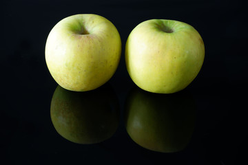 Two ripe juicy yellow apples on black glossy background with reflection