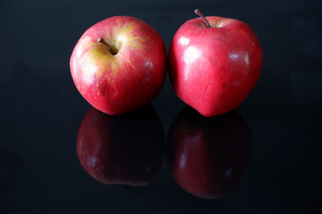 Two ripe fresh red apples on black glossy background with reflection