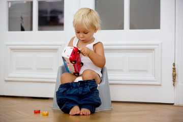 Infant child baby boy toddler sitting on potty, playing with toys in living room