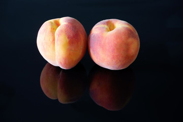 Two fresh juicy orange peaches on black glossy background with reflection