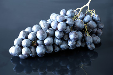 Bunch of dark blue fresh grapes on black glossy background with reflection