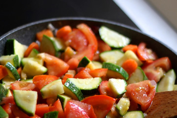 Cooking vegetables in a pan: zucchini, tomato and carrot. Selective focus.