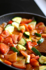 Cooking vegetables in a pan: zucchini, tomato and carrot. Selective focus.