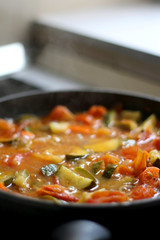 Cooking vegetables in a pan: zucchini, tomato and carrot. Selective focus.