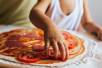 Funny happy chef boy cooking pizza at home at the table