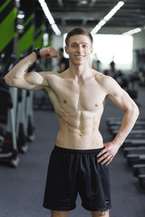 Naklejka na ściany i meble Portrait of sportsman with perfect body standing at the gym after workout and showing his biceps