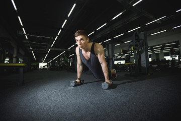 Athletic man doing push-ups with the dumbbells at the gym