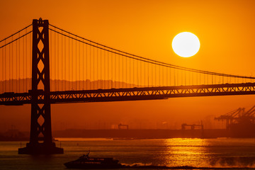Foggy/Misty summer morning sunrise in California and silhouette of the iconic Oakland Bay Bridge in San Francisco as ferry/yacht/boat sails by. Famous travel location landmark in the west coast city.