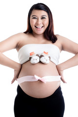 Pregnant woman's belly with baby shoes and ribbon bow