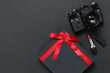 Old retro vintage camera, Black gift box with red ribbon, red lipstick on black background top view flat lay with copy space. Concept for the photographer, old photographic equipment, present