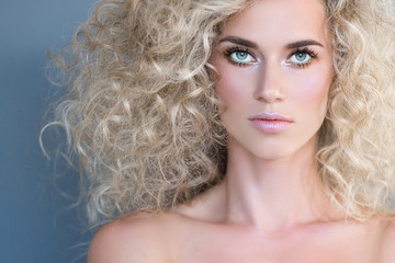 Portrait beautiful sensitive young blonde girl with curly hair and pink radiant skin posing on gray background. Concept of beauty hairstyles cosmetics and glamor. Copyspace. 16 in 9 crop for design