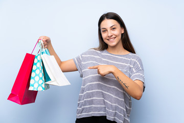 Young brunette woman over isolated blue background holding a lot of shopping bags