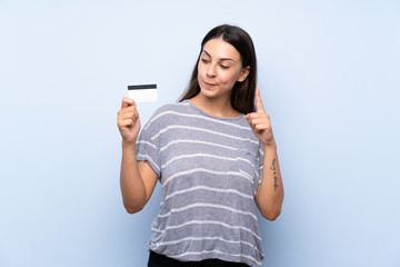 Fototapeta premium Young brunette woman over isolated blue background holding a credit card