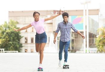 Fototapeta premium Happy teenage couple riding modern cruiser skateboards on city street