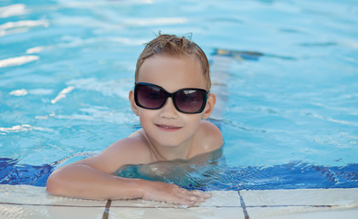 Happy boy with blond hair smiling sitting in swimming pool