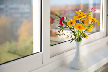 a beautiful autumn bouquet of yellow and purple flowers in a white elegant vase stands on the windowsill. Autumn background. The concept of autumn, sadness. Copy space - Powered by Adobe