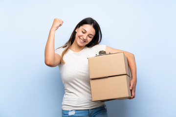 Young delivery woman over blue brick wall celebrating a victory
