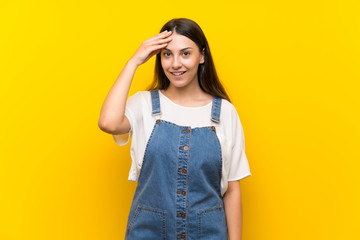 Young woman in dungarees over isolated yellow background has just realized something and has intending the solution
