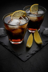 rum and cola Cuba Libre with ice and lemon on dark stone background