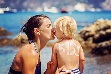 Mother, kissing her toddler child on the beach, sign kiss on his back