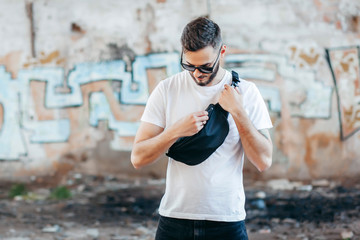 Stylish bearded hipster in the at the city in a white T-shirt with waist bag