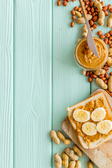 Make sandwiches with banana and peanut butter in glass bowl, knife on mint green wooden background top view copyspace