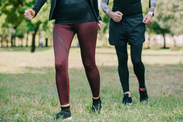 Fototapeta premium cropped view of mature sportsman and sportswoman jogging in park
