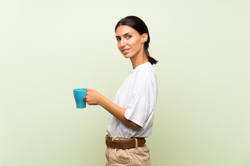 Young woman over isolated green background holding hot cup of coffee