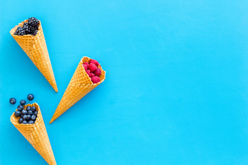 Summer breakfast with fresh berries in waffle cones on blue background top view mockup