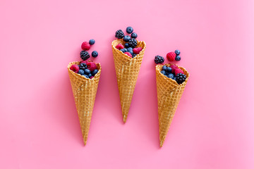 Summer breakfast with fresh berries in waffle cones on pink background top view