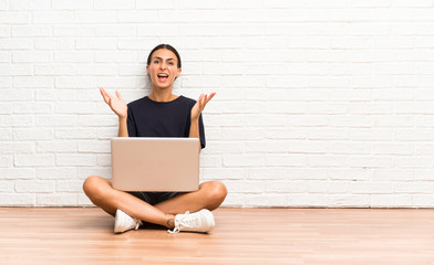 Young woman with a laptop sitting on the floor unhappy and frustrated with something