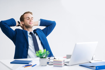 Relaxing or dreaming businessman with hands behind head, in blue suit working with laptop computer...