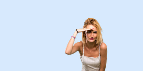 Young blonde woman looking far away with hand to look something over isolated blue background