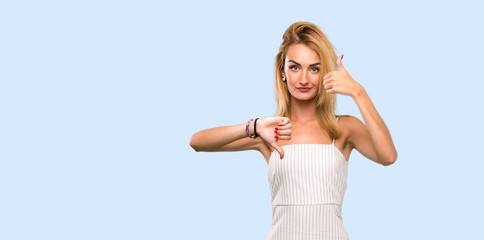 Fototapeta na wymiar Young blonde woman making good-bad sign. Undecided between yes or not over isolated blue background