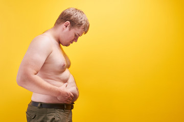 Huge young man with big fat belly and naked body in profile. Concept of obesity, fast and junk...